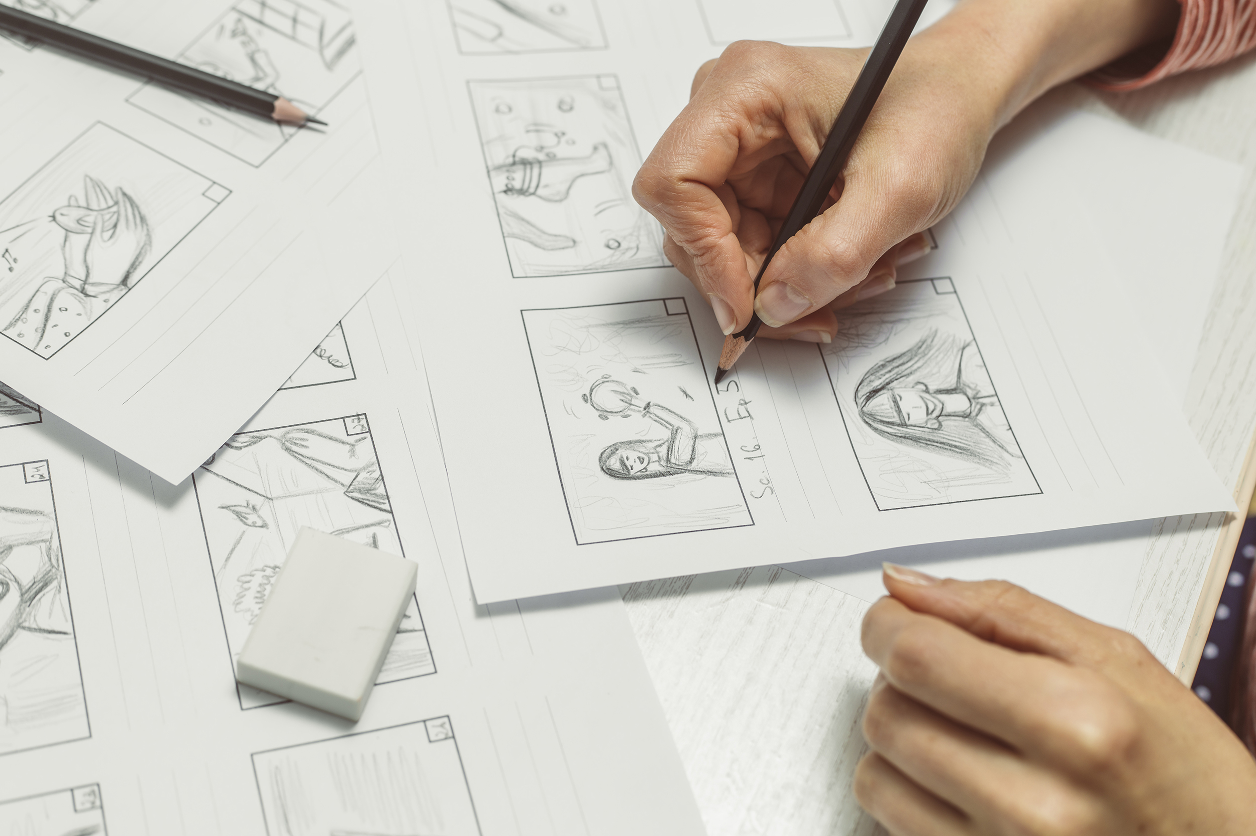 Photo of a hand drawing sketches on paper forming a storyboard.