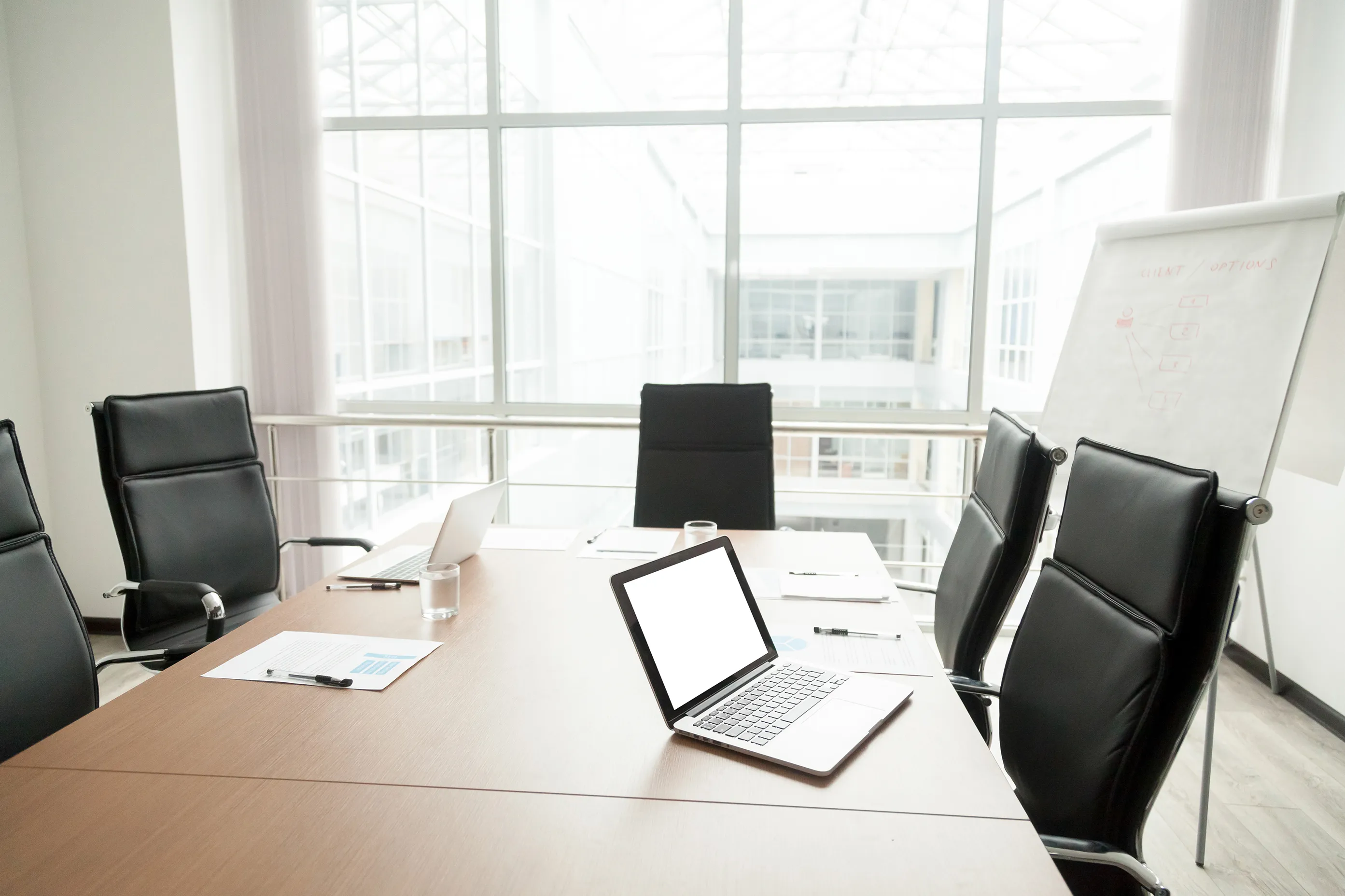 Photo of an empty conference room with an open laptop, blank paper and a presentation-size note board.