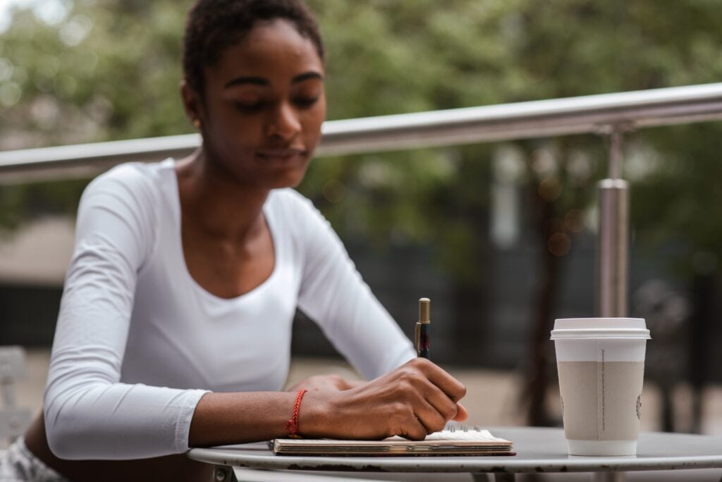 nonprofit consulting palm desert ca with woman sitting at a table with coffee, writing. Maybe she's preparing a budget for her new nonprofit startup!