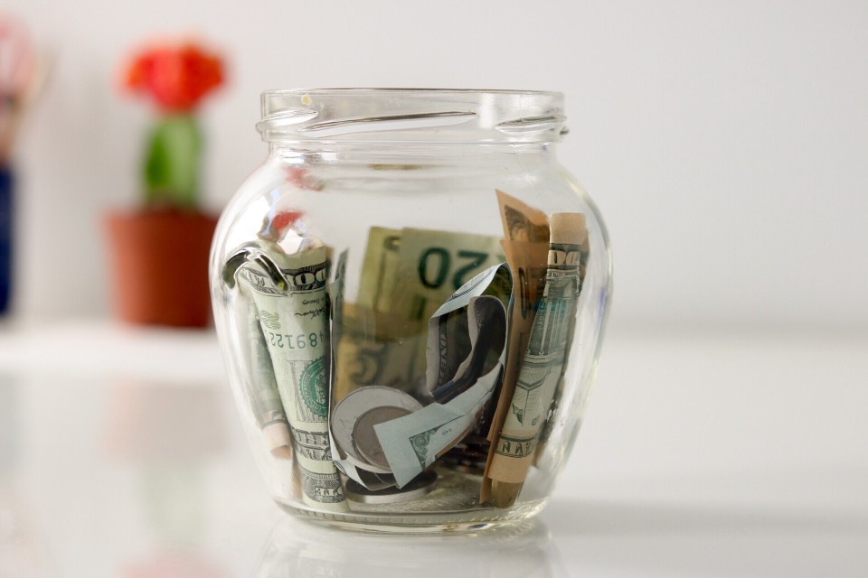 A glass jar filled with paper money and coins sits on a white desk ready to be incorporated into an organization's fundraising system!