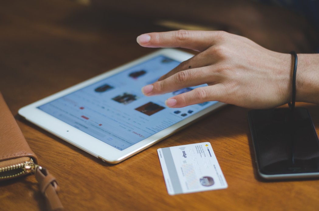 A tablet lies flat on a desk with a hand poised above it, ready to tap. There is a credit card beside it on the desk. Online fundraising systems are crucial to your organization's strategy.