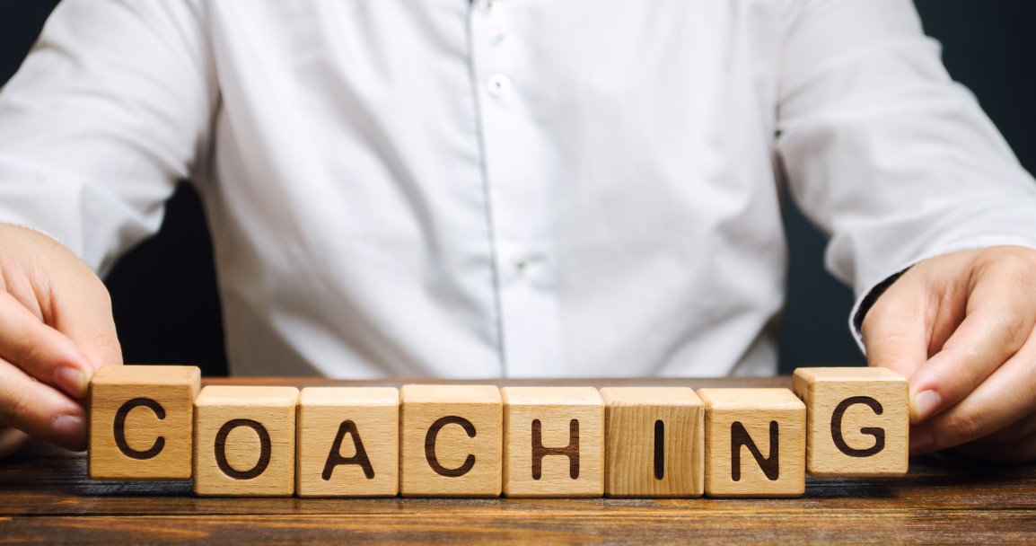 A nonprofit career coach holds wooden letter blocks that say "COACHING." He is wearing a white shirt. We see only his hands.