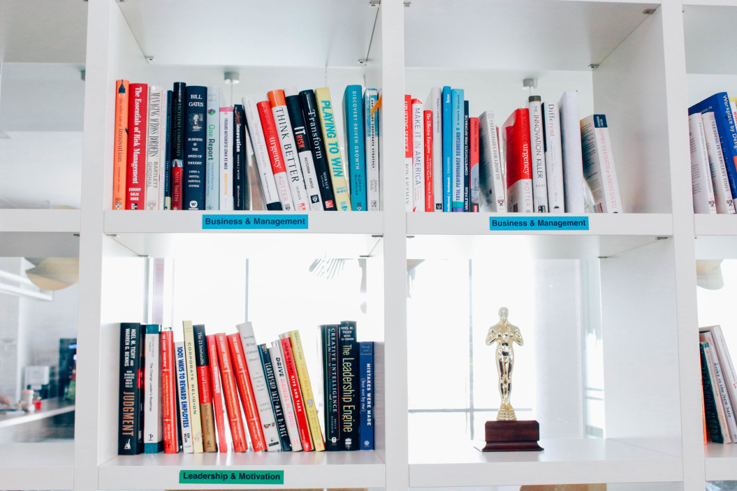 A glossy white bookcase with open cubbies is full of books on nonprofit marketing. There is a sole, gold trophy on a small wooden base on a shelf in the lower right corner.