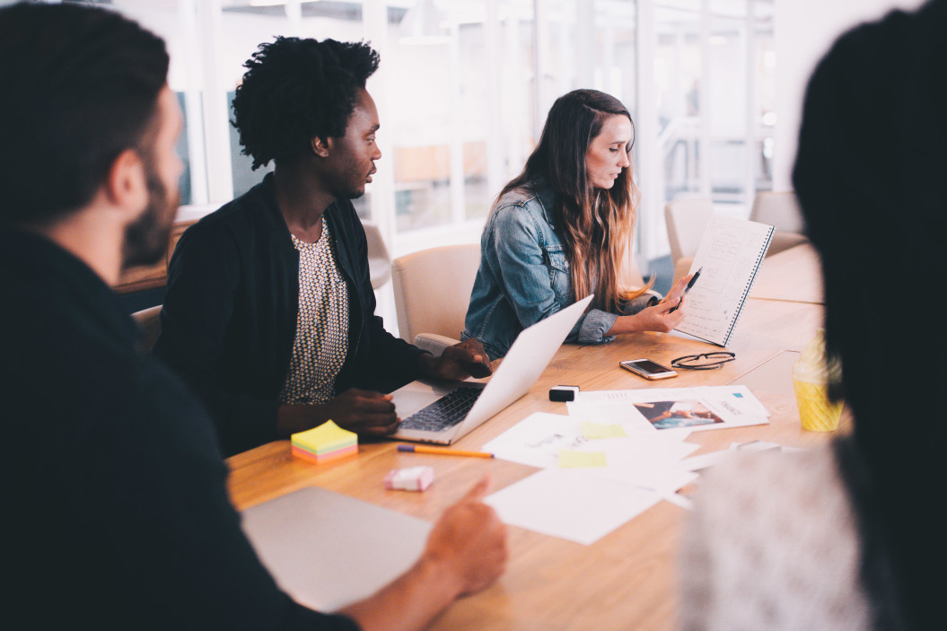 Several people sit around a table for a nonprofit board development session. One man sits in front of a laptop. The woman next to him holds up a notebook.