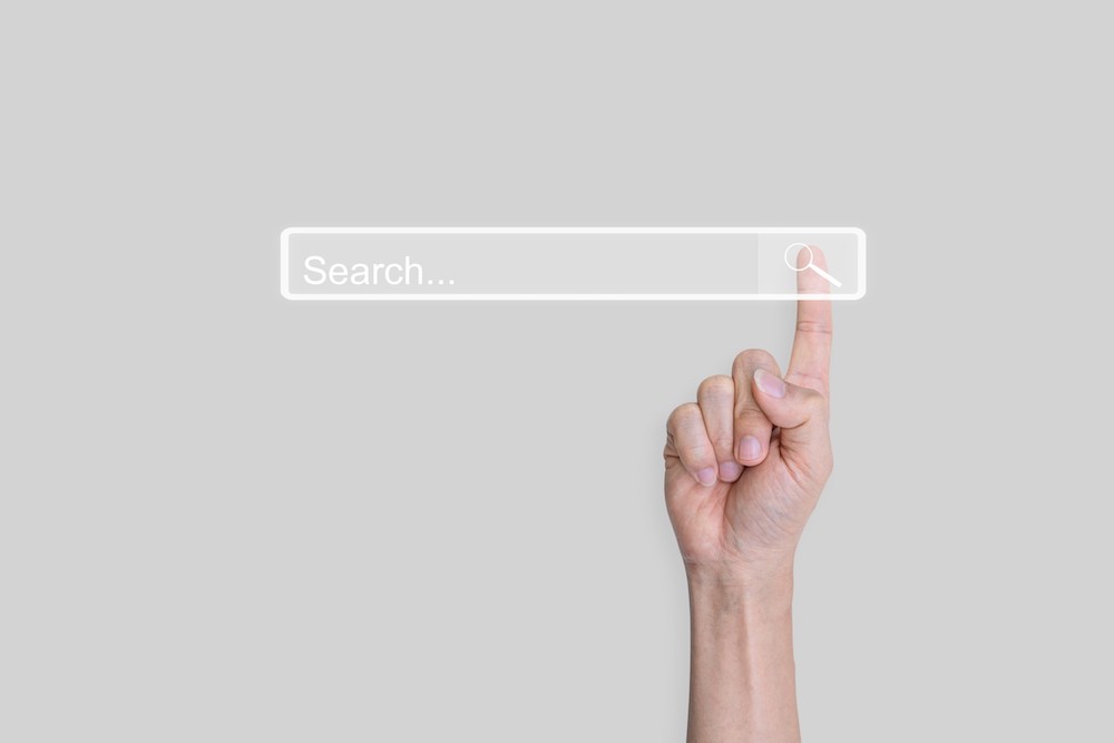 A fist comes up from the bottom of the frame with an index finger pressing a search button. It's important for organizations to understand SEO basics for nonprofits.