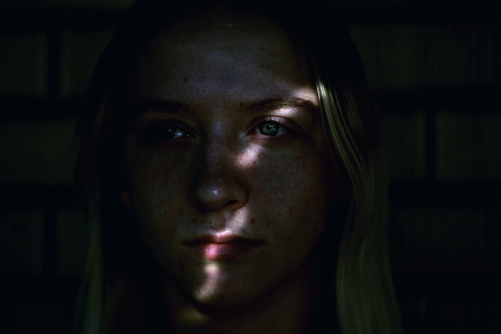 A young woman struggling with Seasonal Affective Disorder stands alone in the dark. Her face is illuminated by a sliver of light.