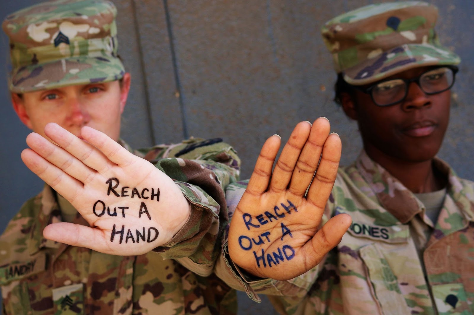 Two members of the military have the words "reach out a hand" written on their palms.