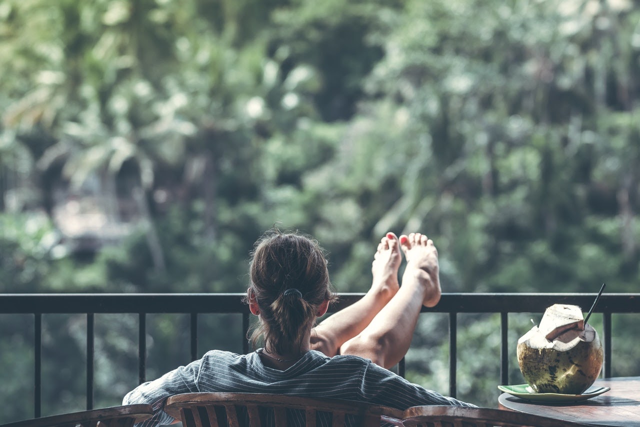 A woman sits on a porch with her legs up, leaning back in a chair. She appears carefree and without much anxiety.