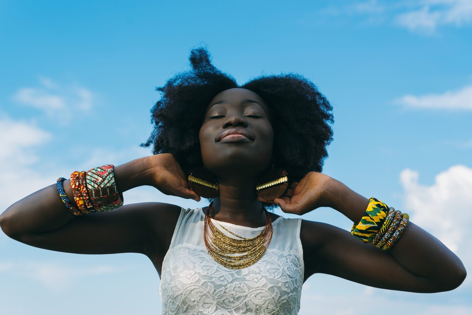 Smiling woman with eyes closed tips her head up towards the blue sky