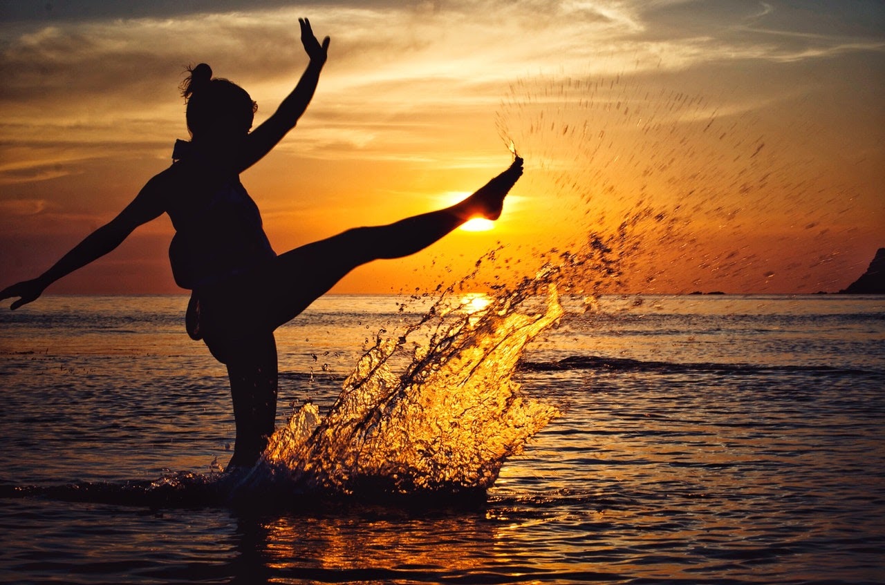 Happy woman kicking up ocean water at the beach with a sunset