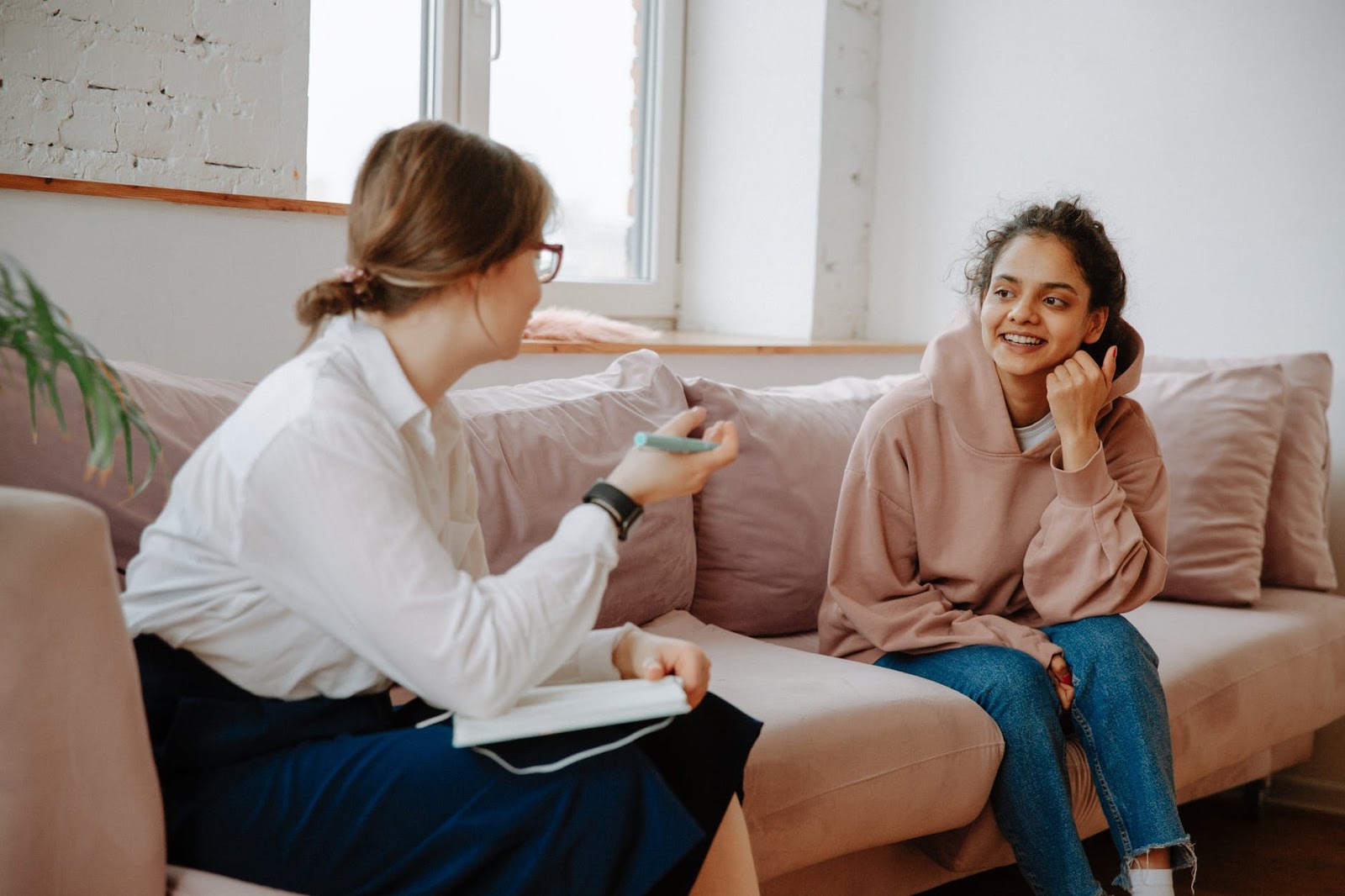 A doctor and patient, both women, talking on a pink couch