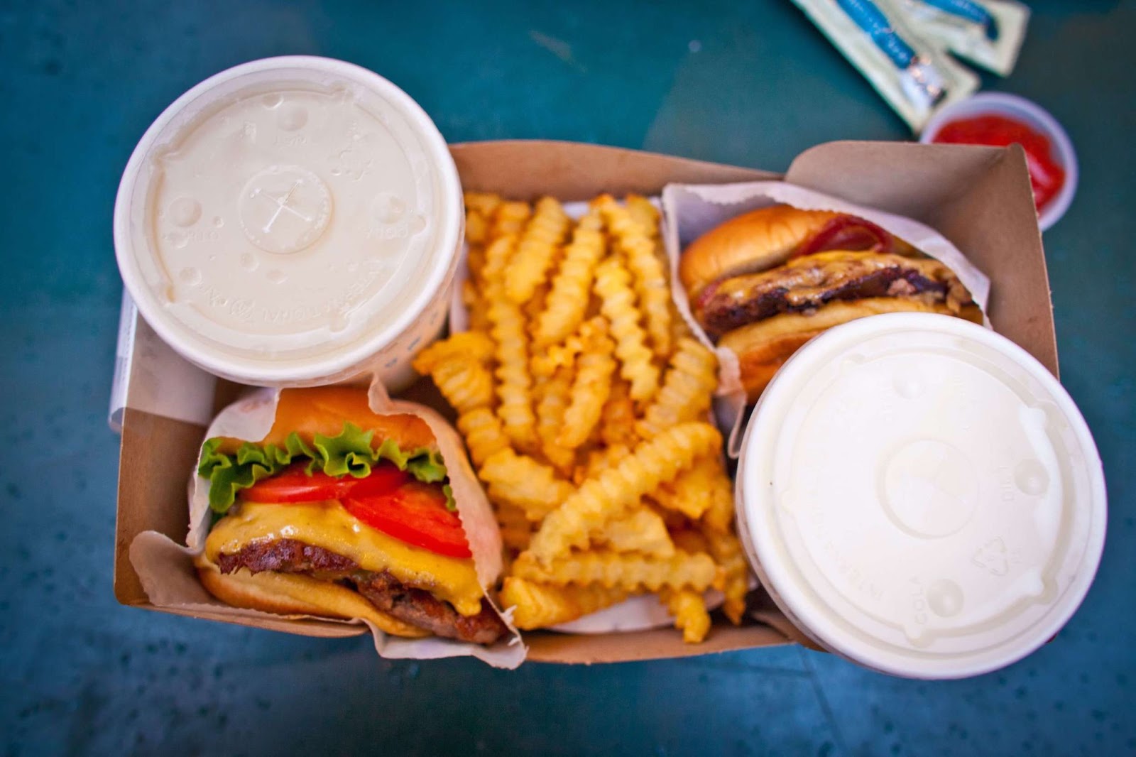 two cheeseburgers, two drinks, and a side of french fries in a cardboard box on a blue table