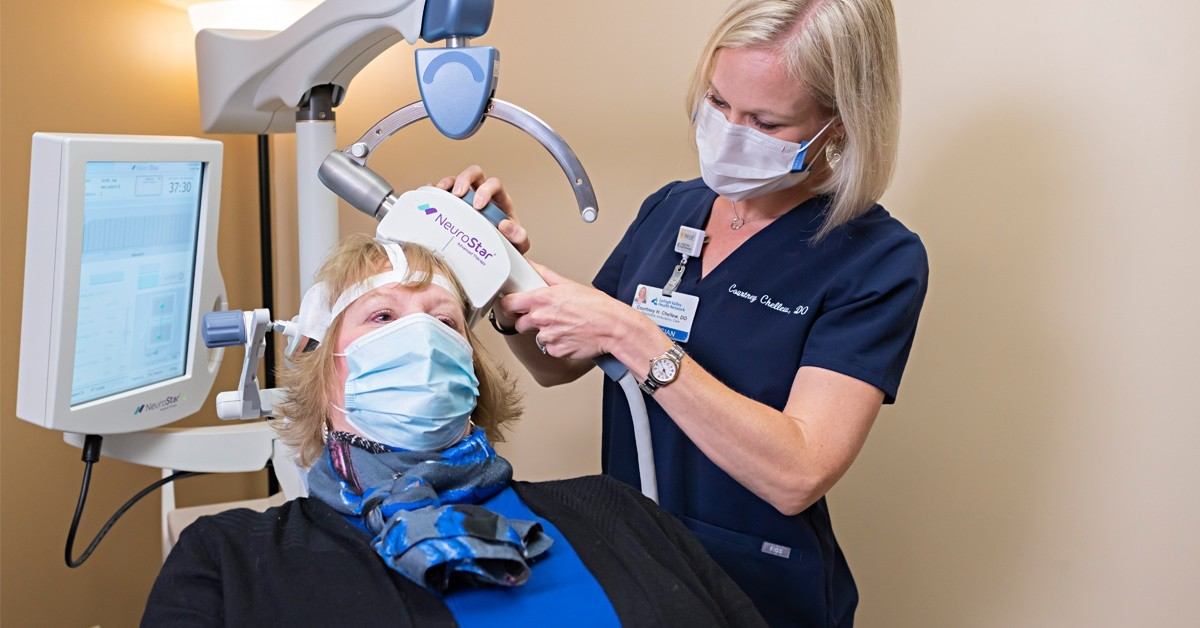 An image of a doctor giving a patient TMS therapy treatment with a machine labeled NeuroStar. Both doctor and patient are wearing COVID safe masks.