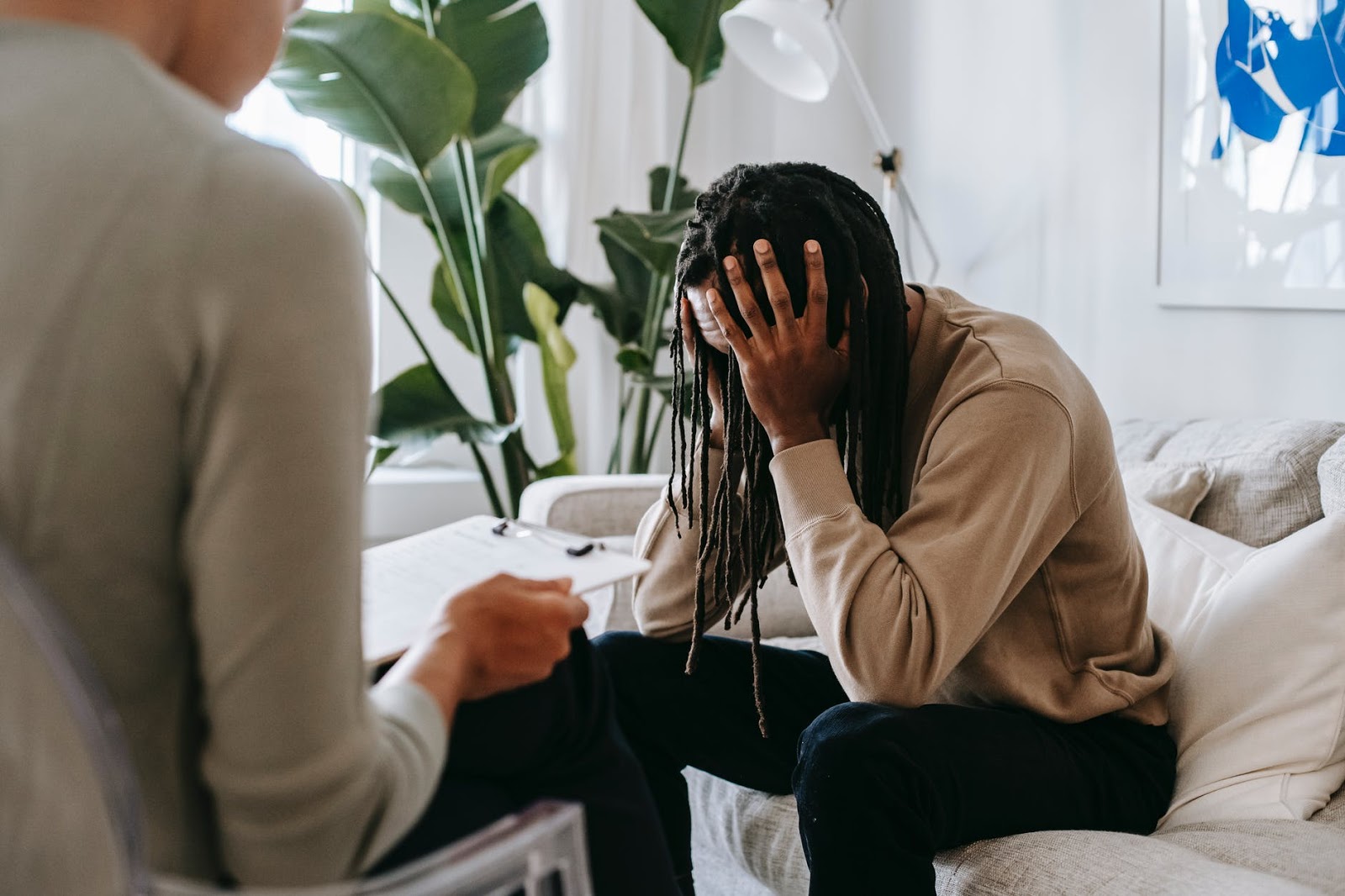 A man with his hands on his head sits on a couch in a therapist's office.