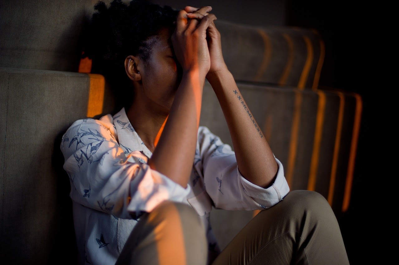 A woman sits with her hands over her face, appearing to be depressed and frustrated.