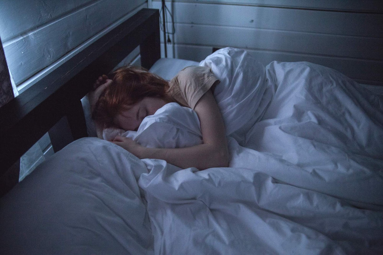 A red-haired woman asleep in a bed with white sheets