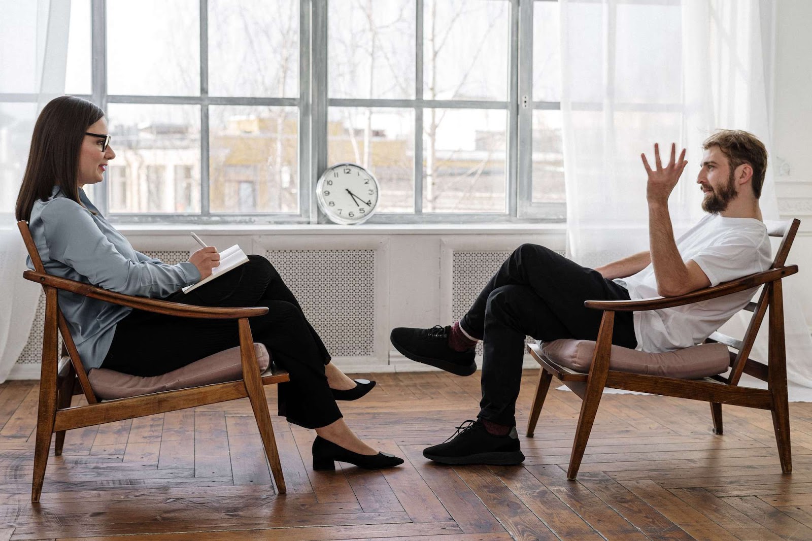 A patient, male, and a therapist, female, talking in a brightly lit room.