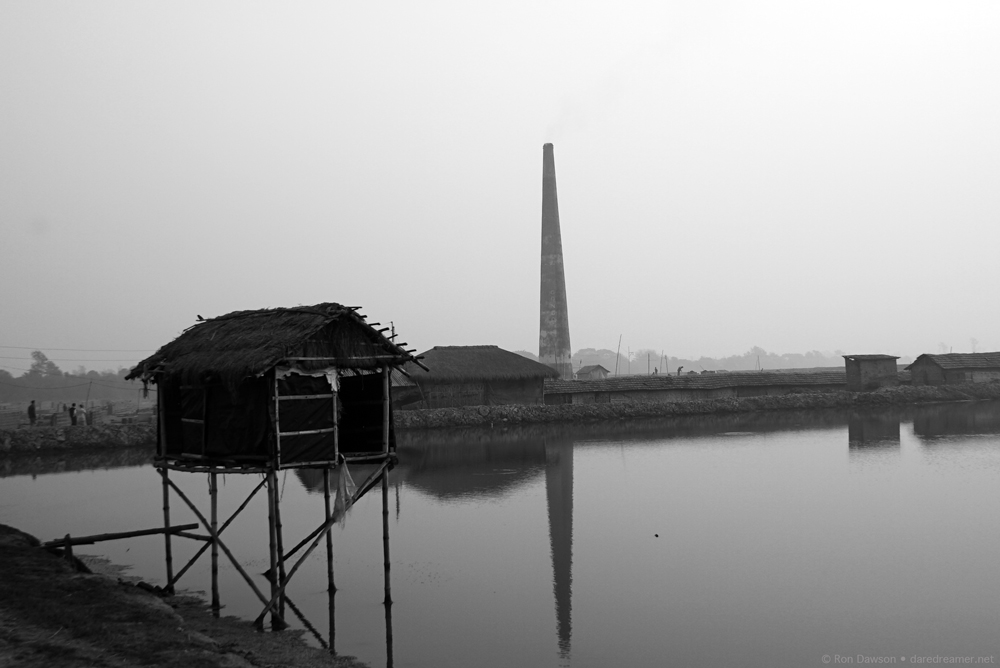 Hut stilt house with factory in background.