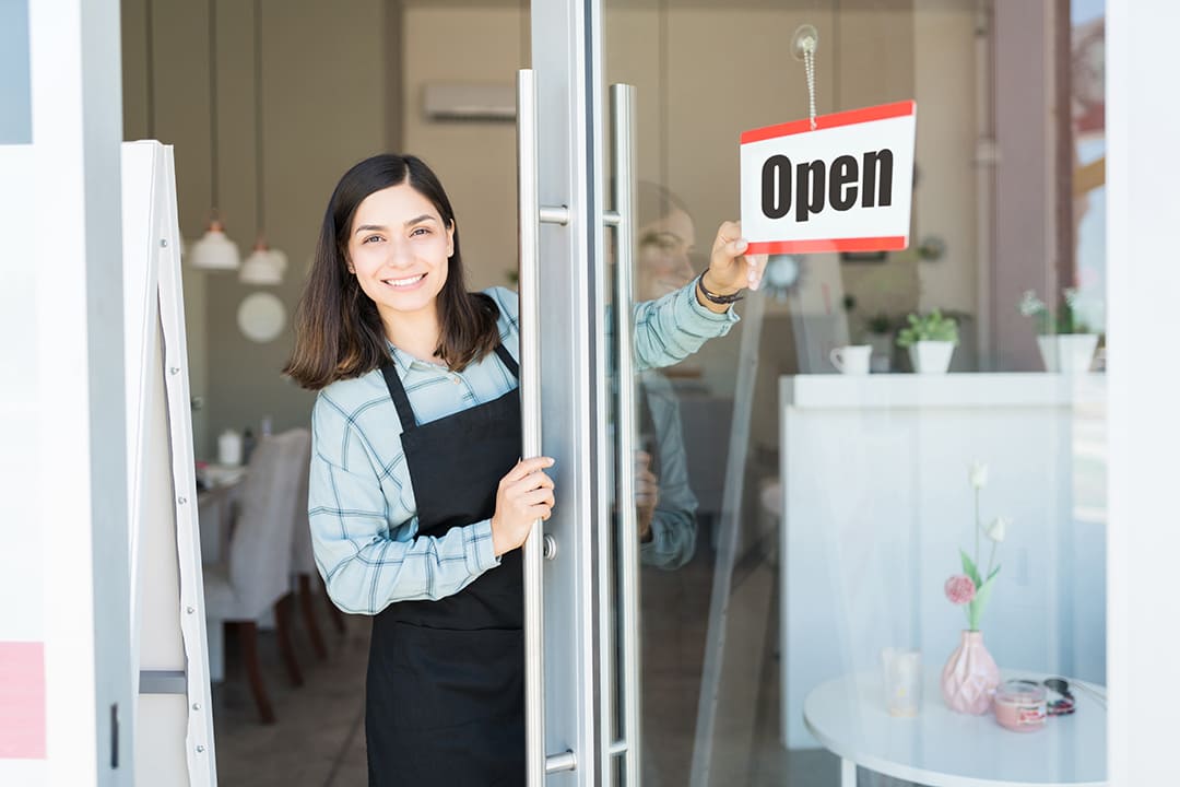 Smiling confident owner turning open sign on glass door of spa