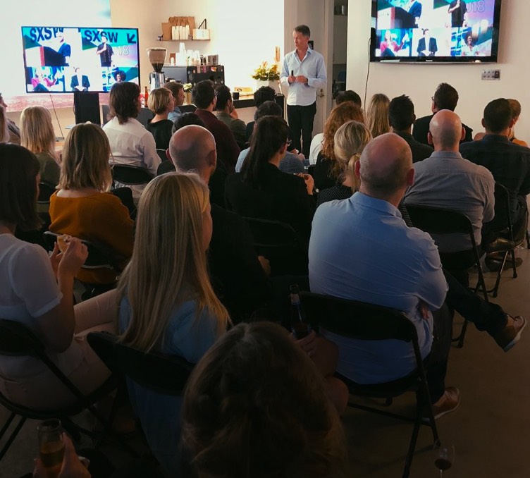 A man presenting insights from SXSW to interested clients and staff.