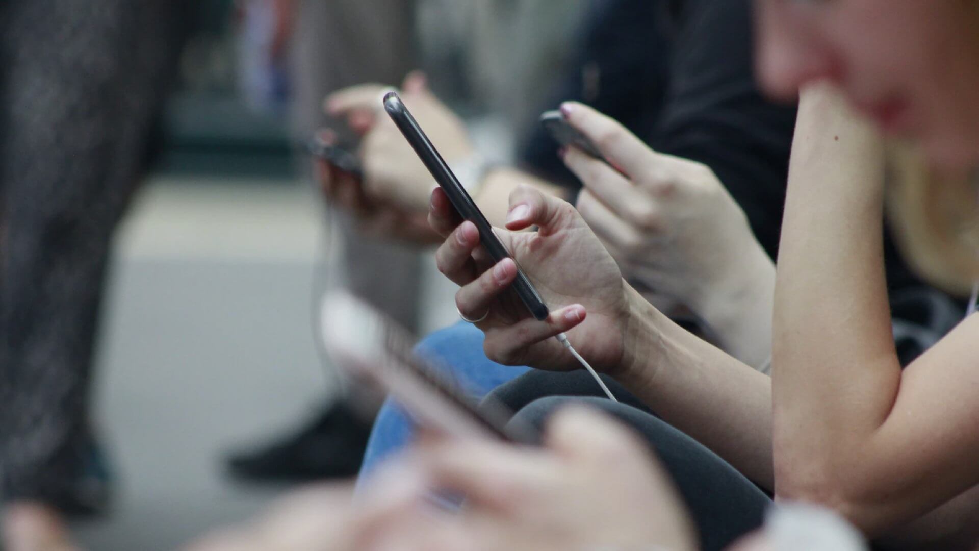 A queue of people seated outdoors, scrolling on their smart phones