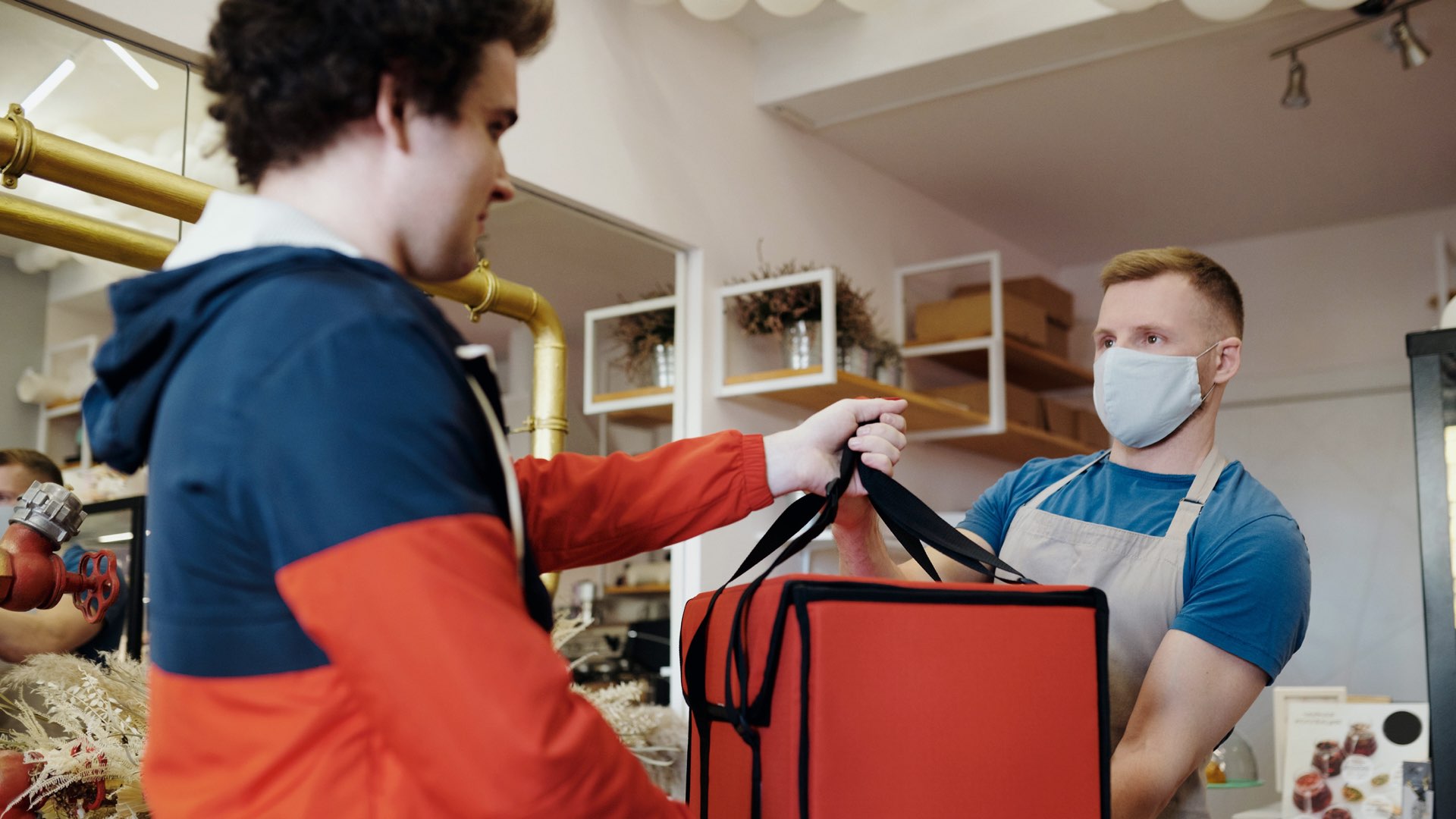 A shop owner handing a food delivery order over to the delivery rider in an insulated bag