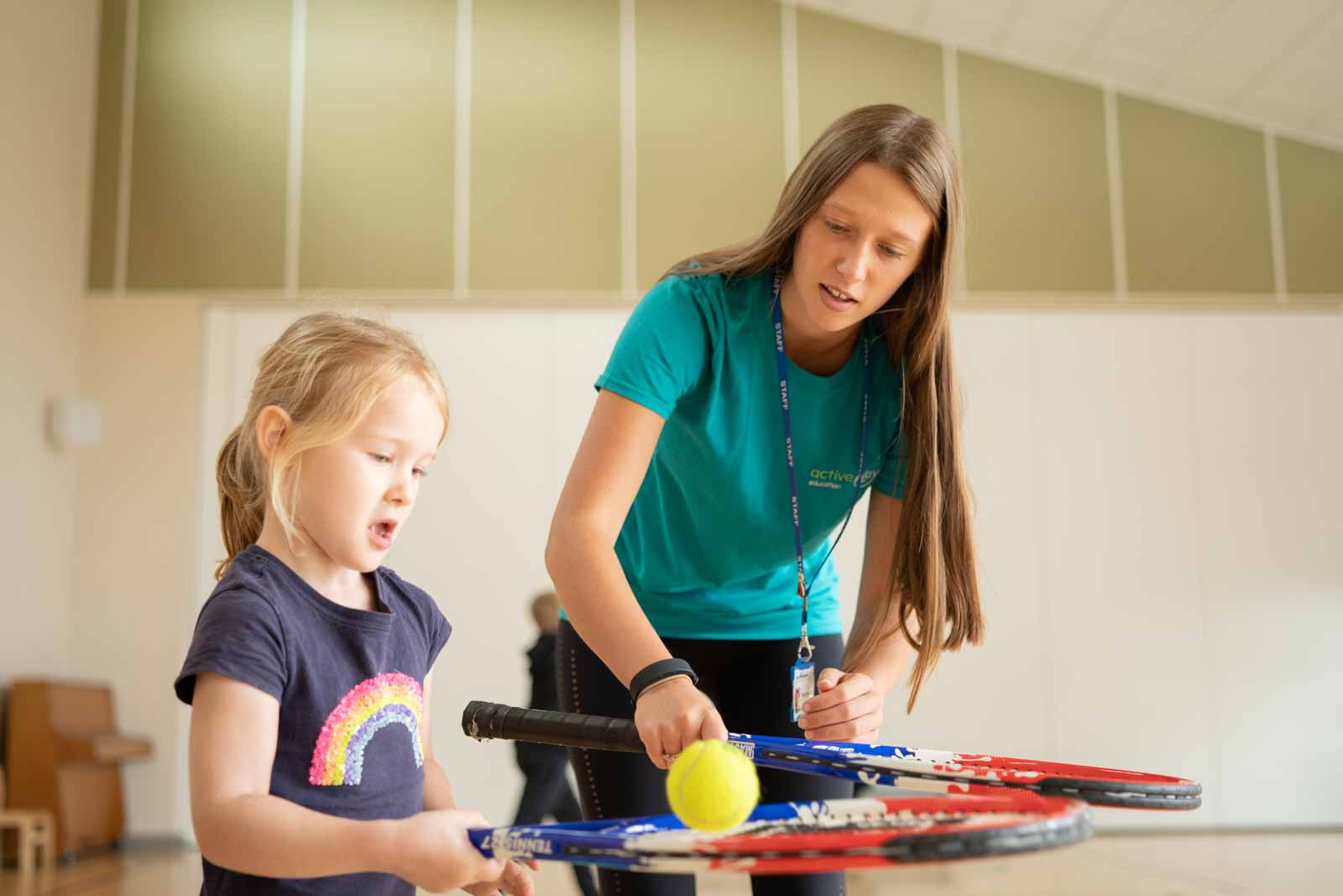 Coach teaching a child to balance a tennis ball on a racket.