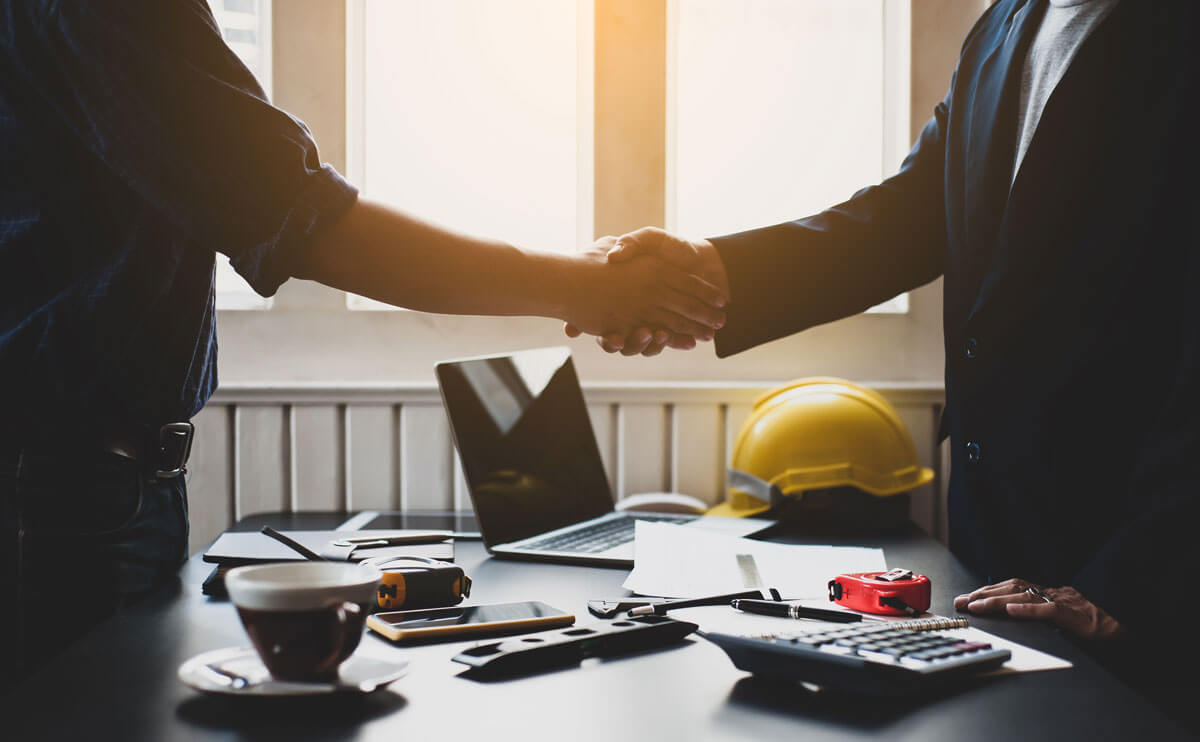 A contractor and owner shake hands at a progress monitoring and reporting meeting.