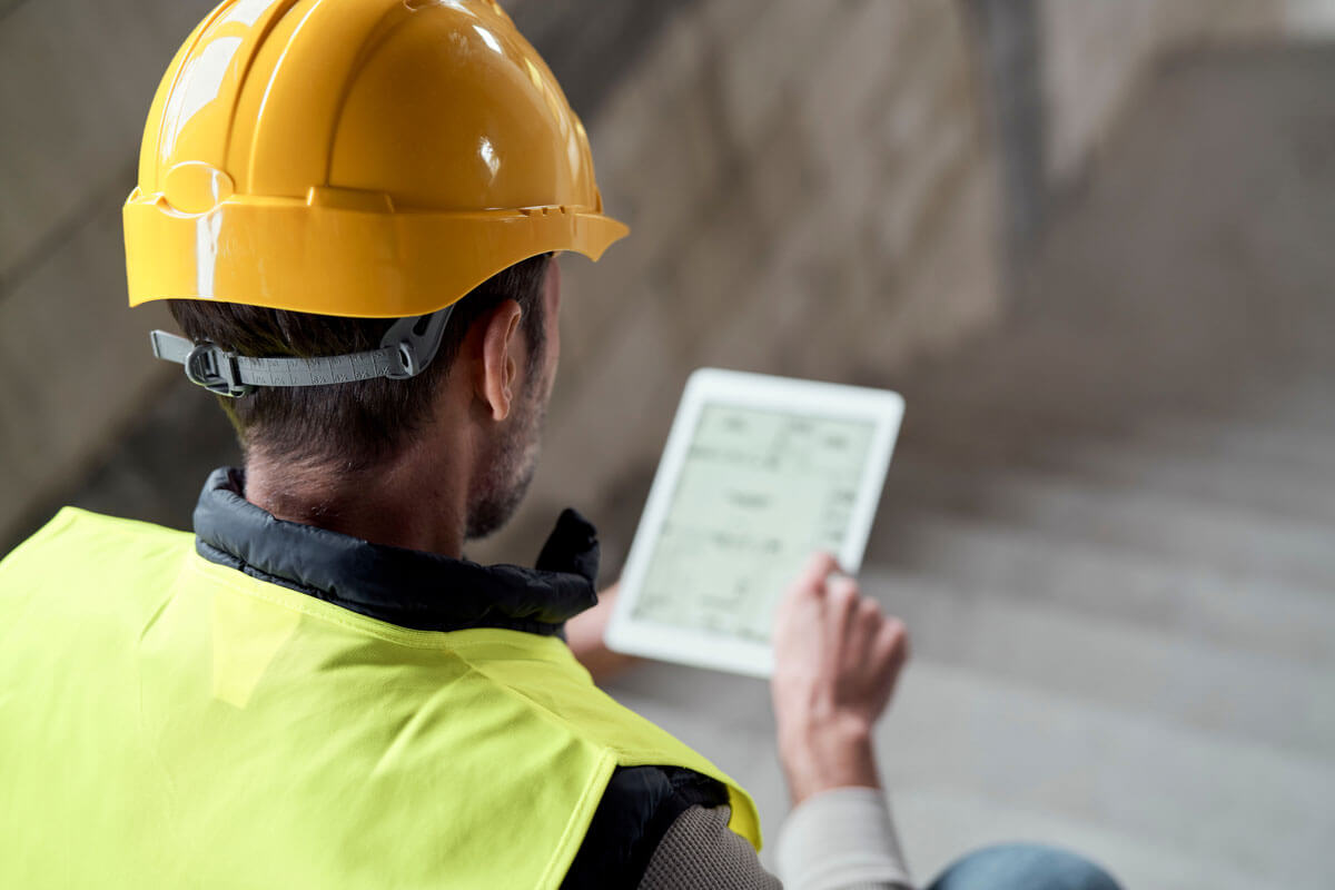 A construction worker files a construction progress report on a tablet.
