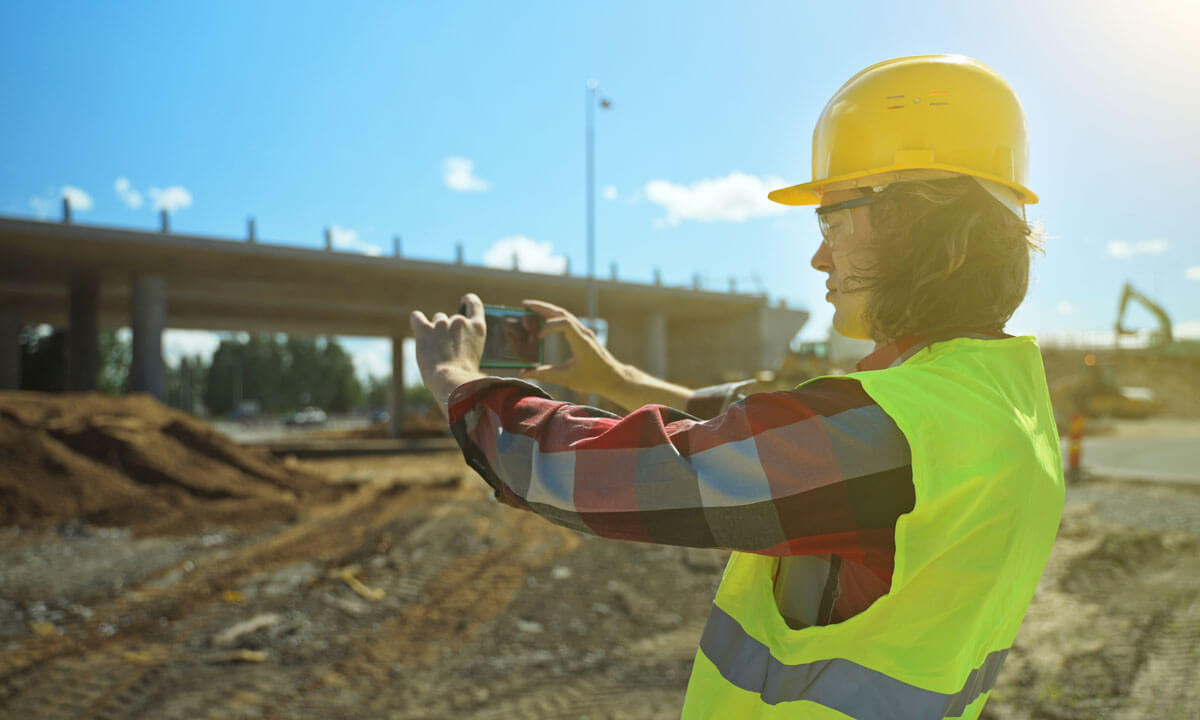 A construction worker uses a smartphone to take construction progress photos.