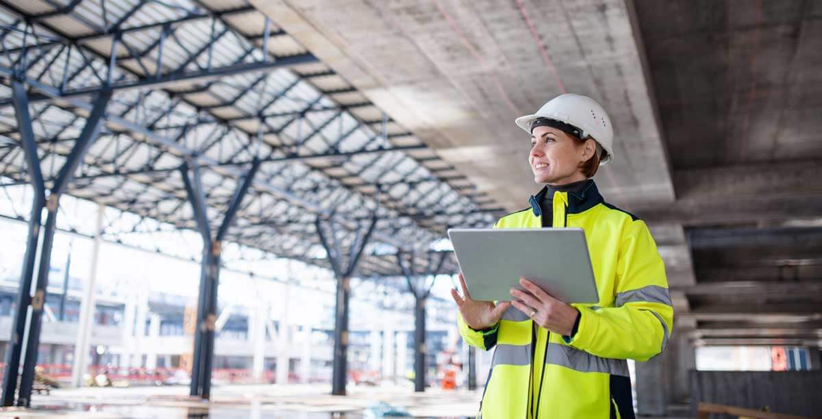 An inspector fills out a construction field report on a tablet at a construction site.