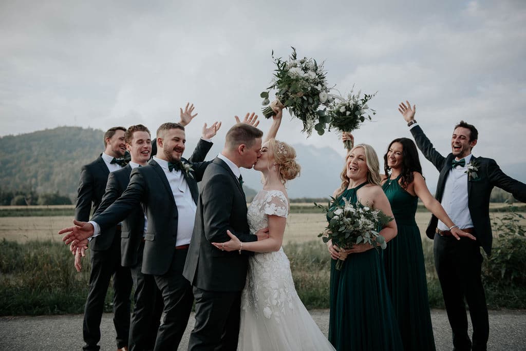 Wedding party posing for photos while bride and groom kiss