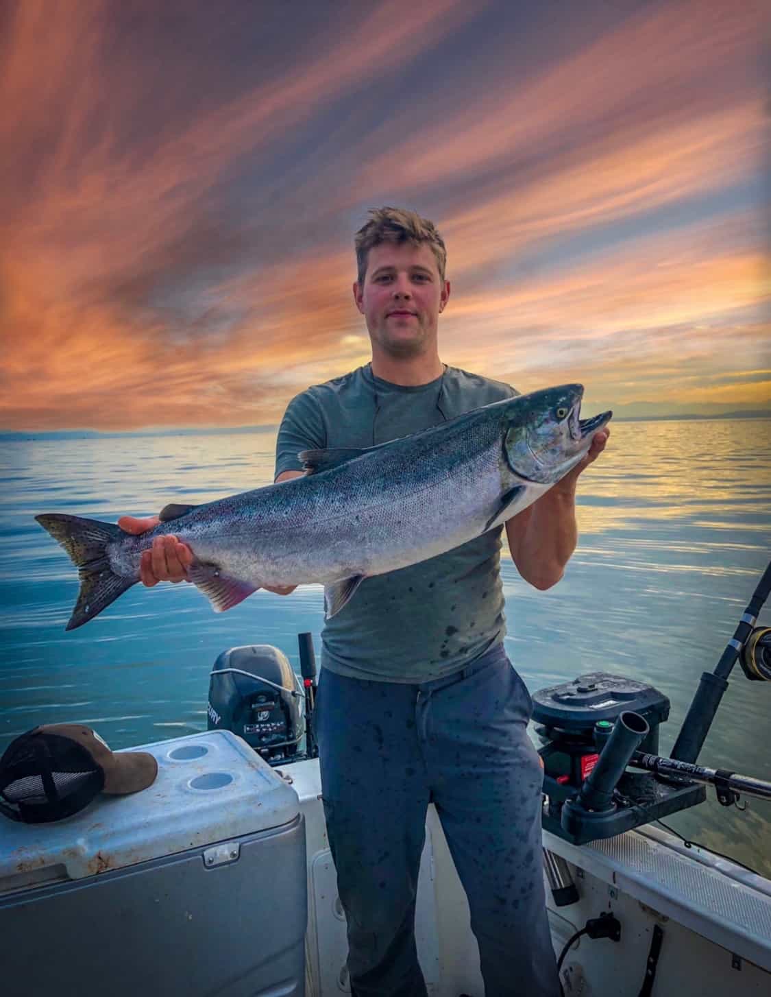 A man holding a fish up on a boat with a sunset
