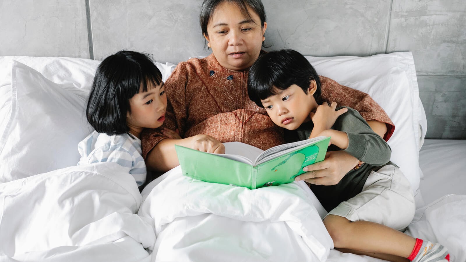 mother reading a bedtime story to her son and daughter in bed