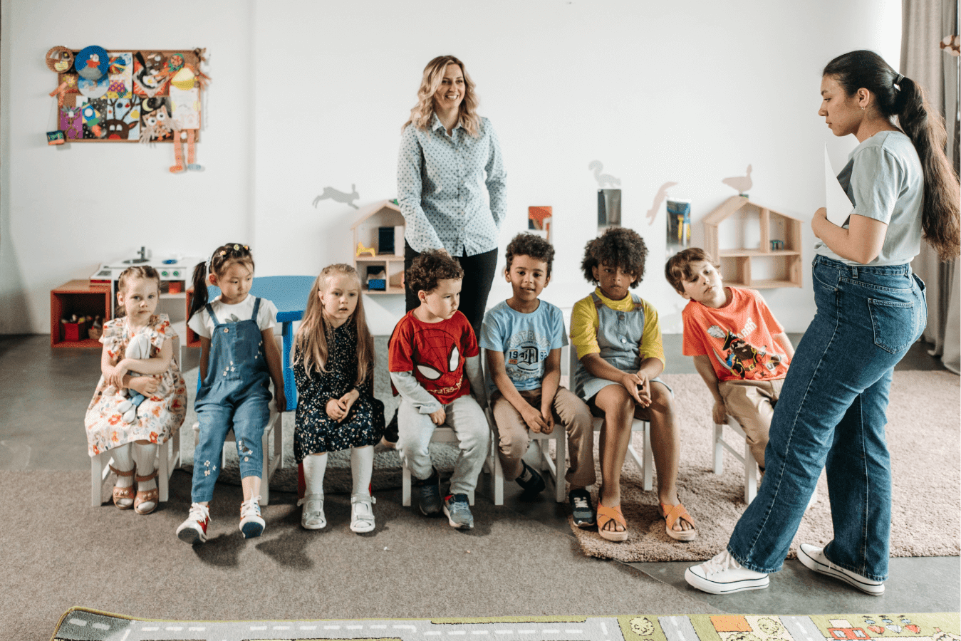 a group of 7 children and two teachers, children sat in a row listening to the teacher