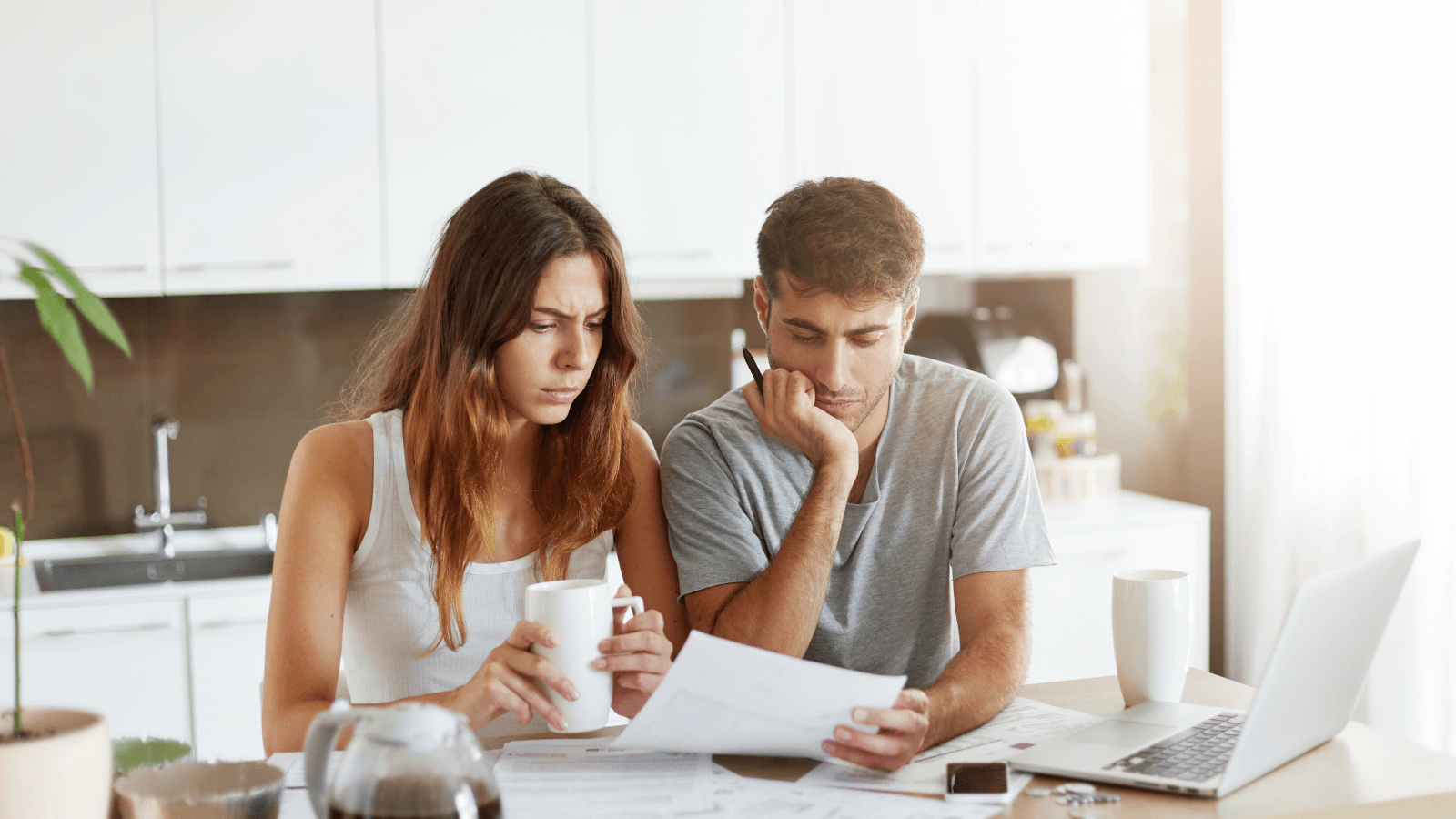 a young couple at the kitchen table with worried faces looking through their bills