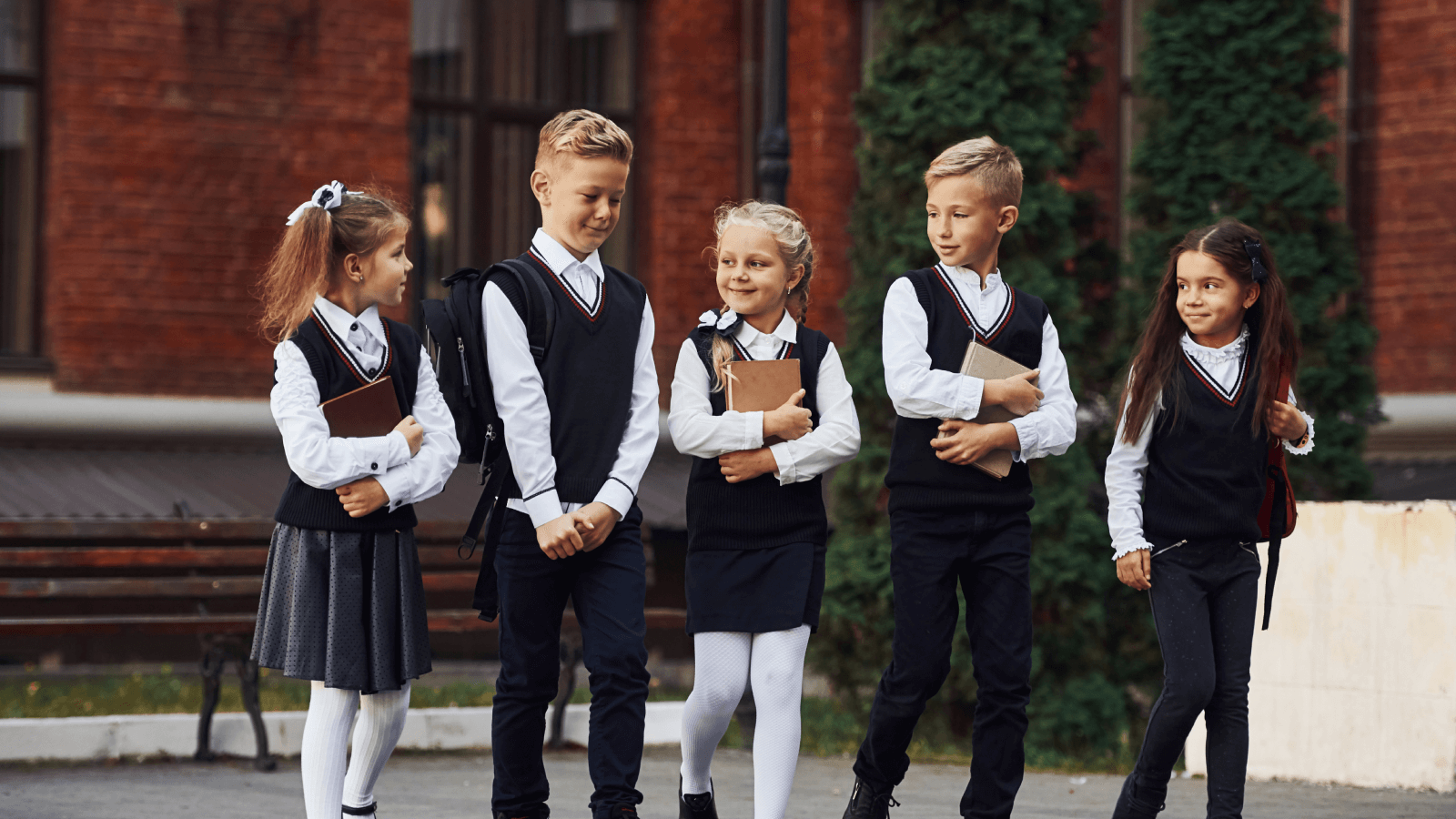 group of school children in their school uniform holding books walking out of school