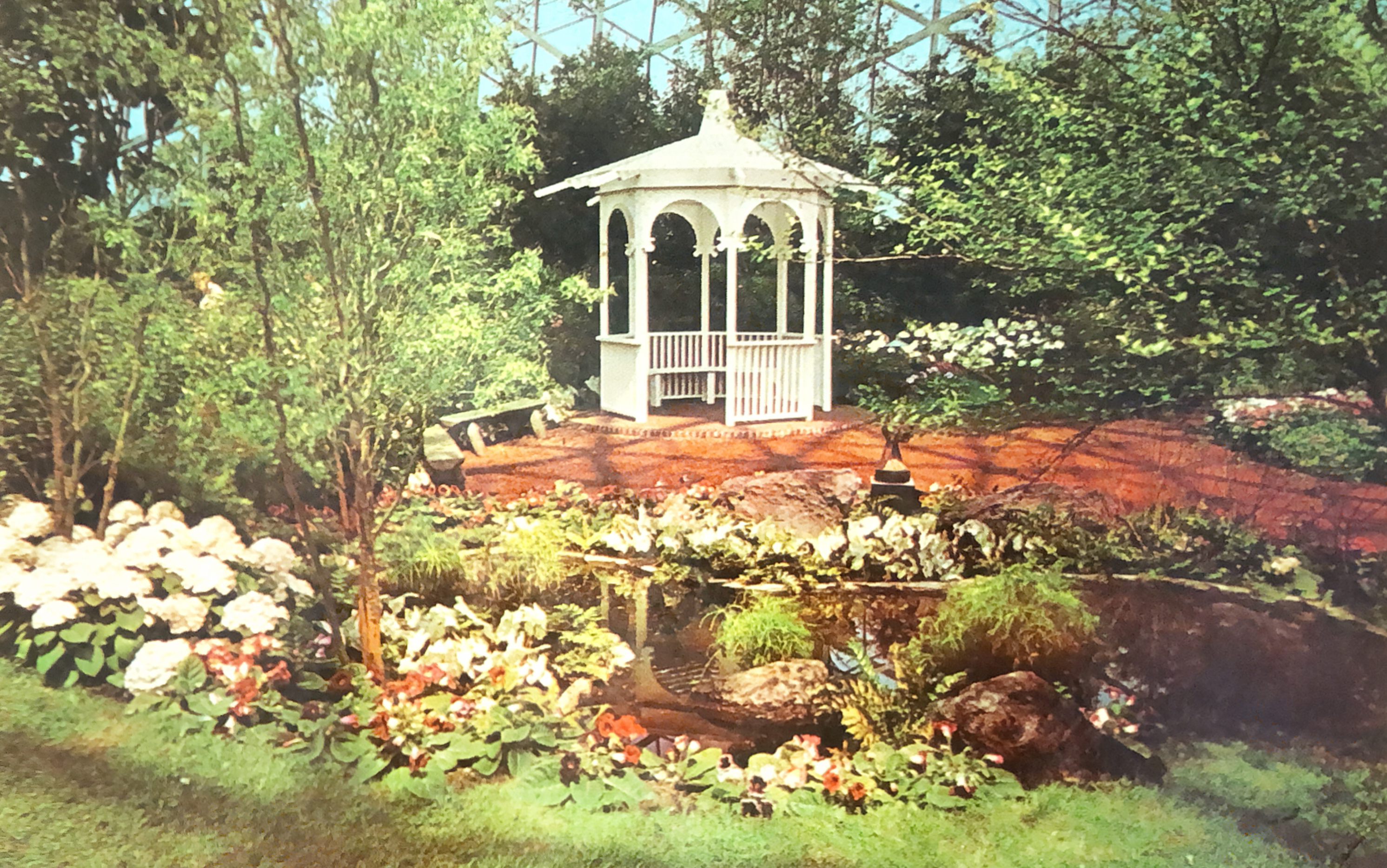 a white gazebo surrounded by plants, stands next to a small pond inside the Show Dome