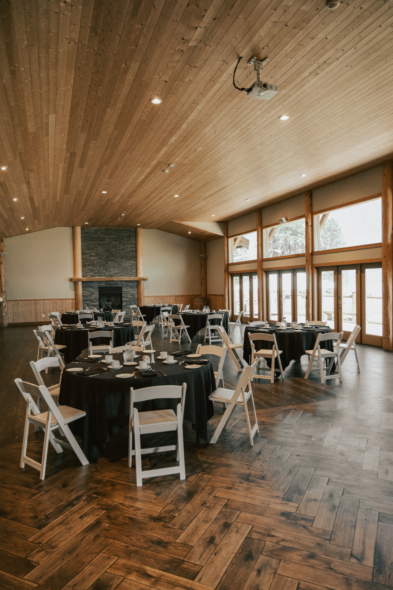 Round meeting tables with black table clothes set up in our log main hall for a corporate event, with white chairs and notepads. The sunlight streaming in from the floor to ceiling windows on the right of the room.