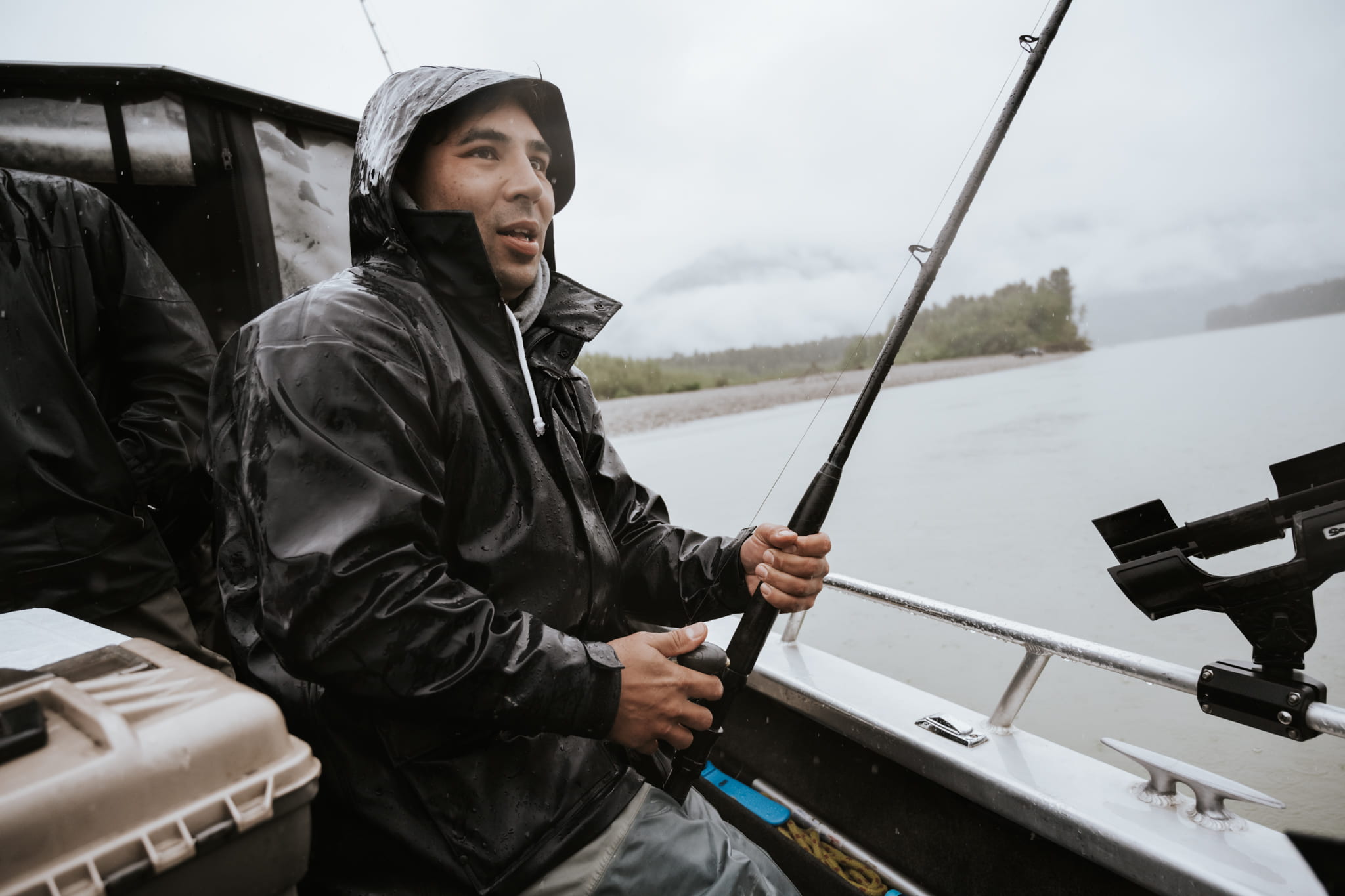 A man standing in a boat while reeling in a sturgeon.