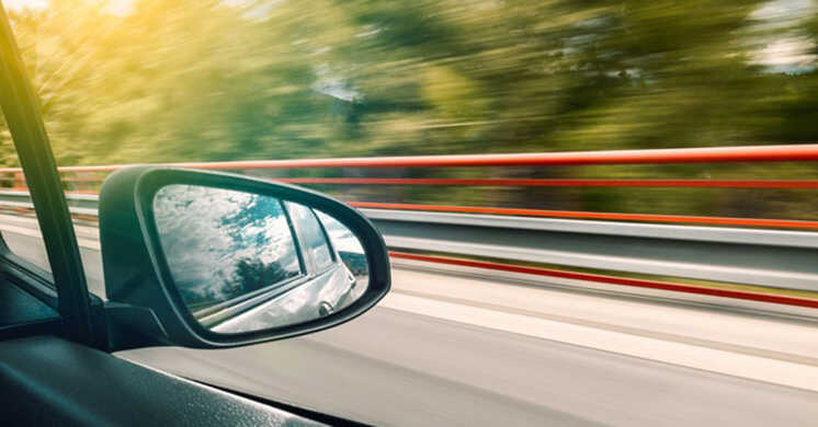 View of vehicle side mirror with blurred ridge railing and background