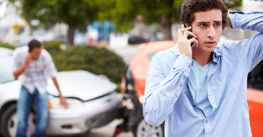 Worried man talking on a cell phone in front of two vehicles that have been in an accident