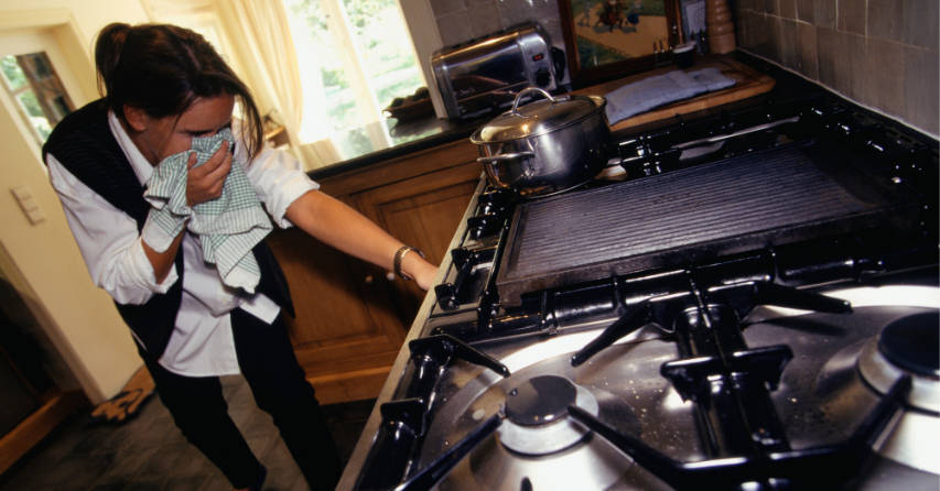 Woman holding cloth over her face while turning off leaking gas in oven