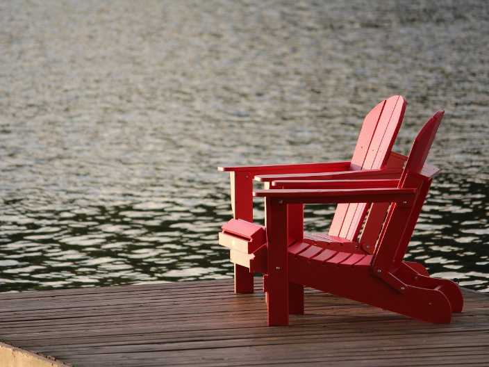 two red muskoka chairs on a dock in a lake