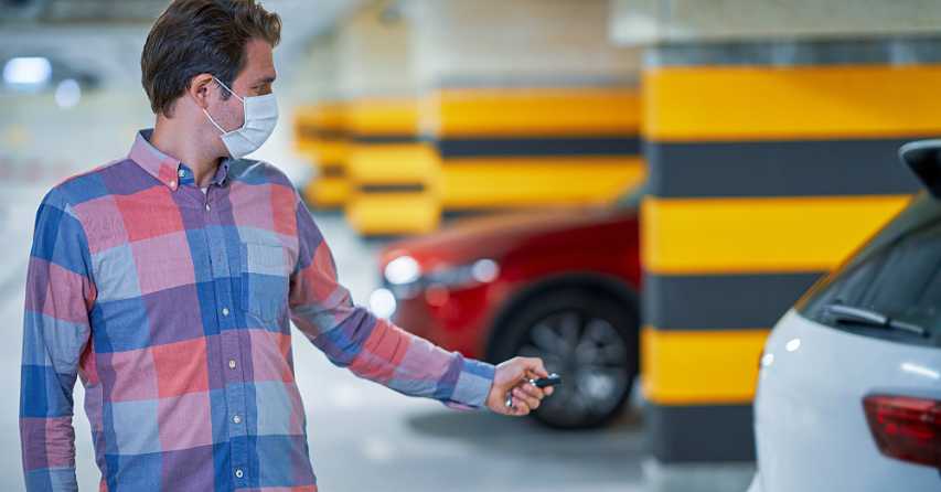 man pointing a keyfob at a vehicle as he walks away