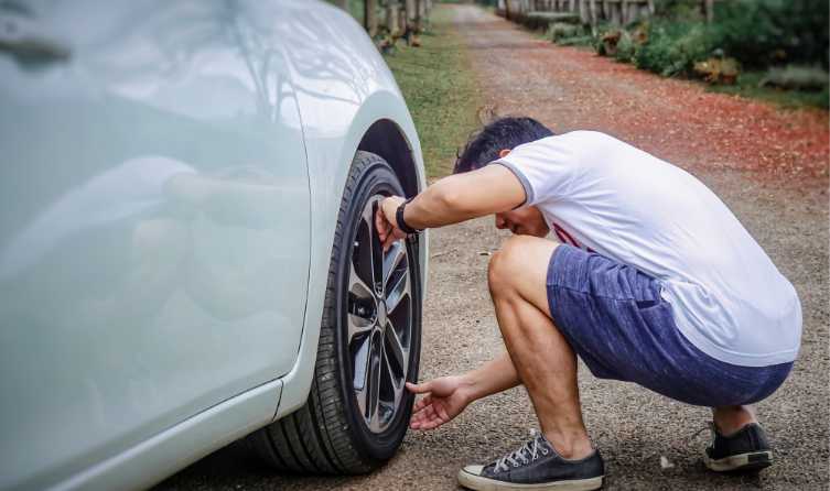 man squatting beside vehicle checking tires for tread wear