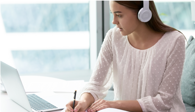 woman jotting down notes on paper in front of laptop listening in to call