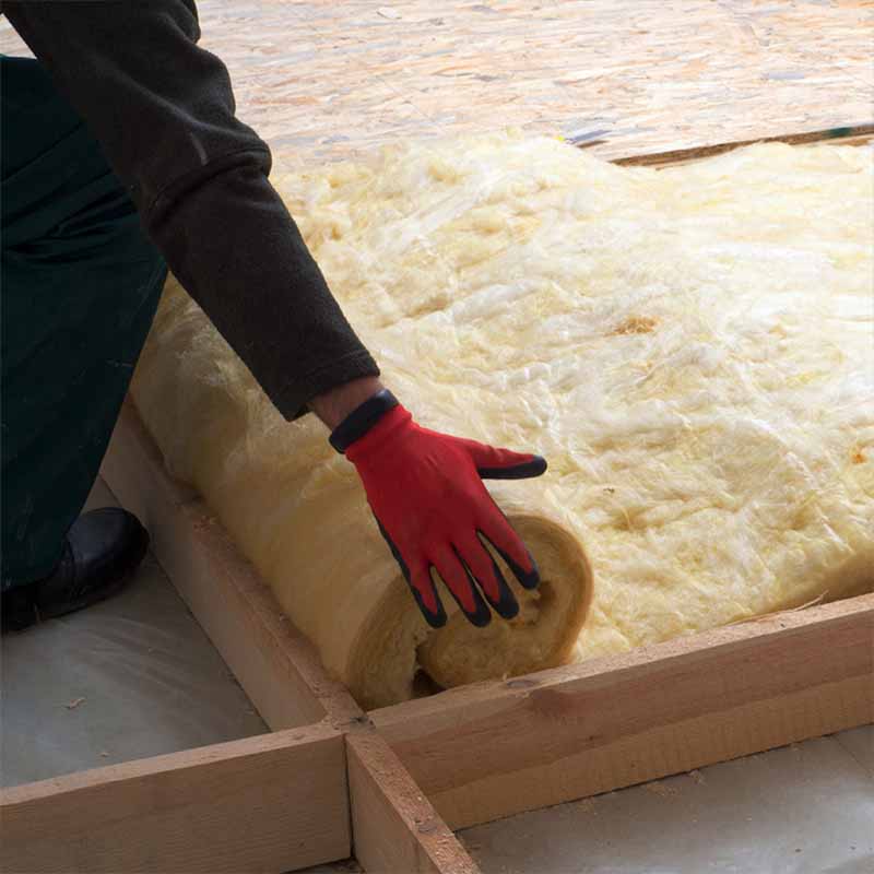 Contractor unrolling fiberglass insulation in the floor joist