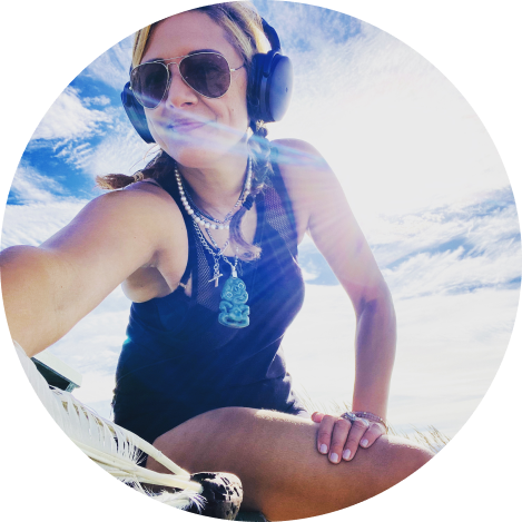 A women with glasses and headphones on, sitting on the beach