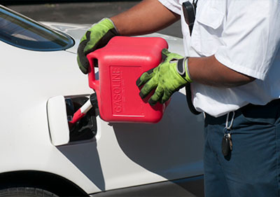 man using a red portable gas can to refuel a white car